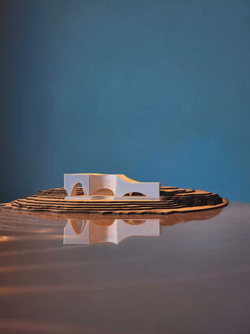 A photograph of the site model, which situates the pavilion on the tip of Macquarie Point. The form of the arched facade is reflected against a dramatic, stilled ocean.