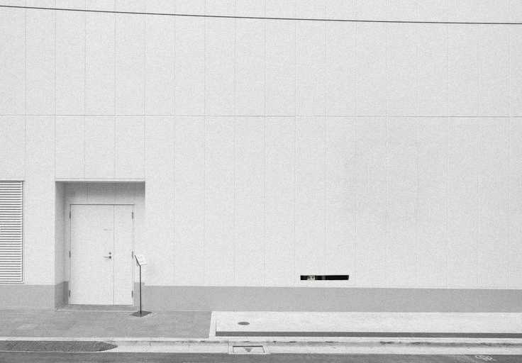 A blank facade with a narrow opening where Oba Yozo peeks out, capturing his cautious, fragmented attempts to watch the world while remaining hidden.